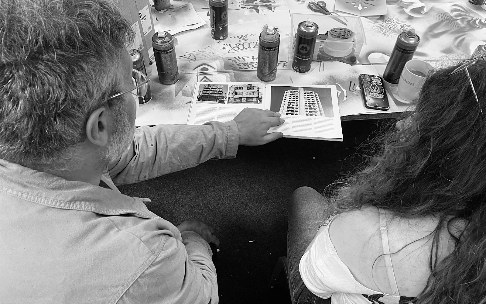 An older artist shows a younger artist a book which is about graffiti