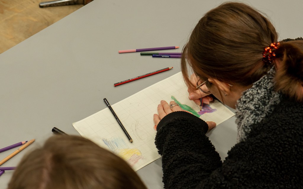 A student draws a picture on a piece of paper with coloured pens