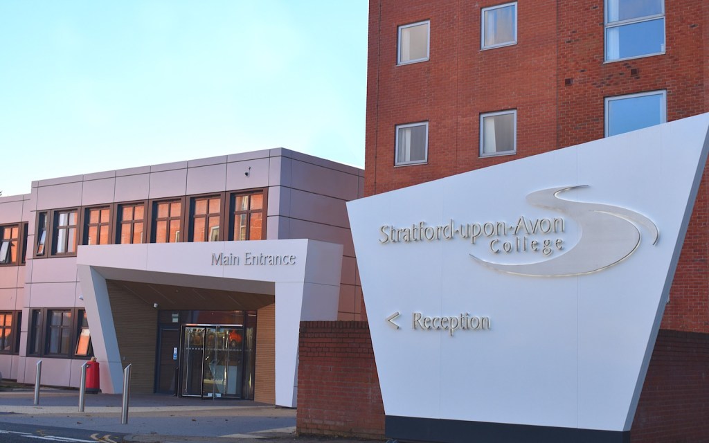 The outside of a college in Stratford-upon-Avon has brick walls and a white entrance