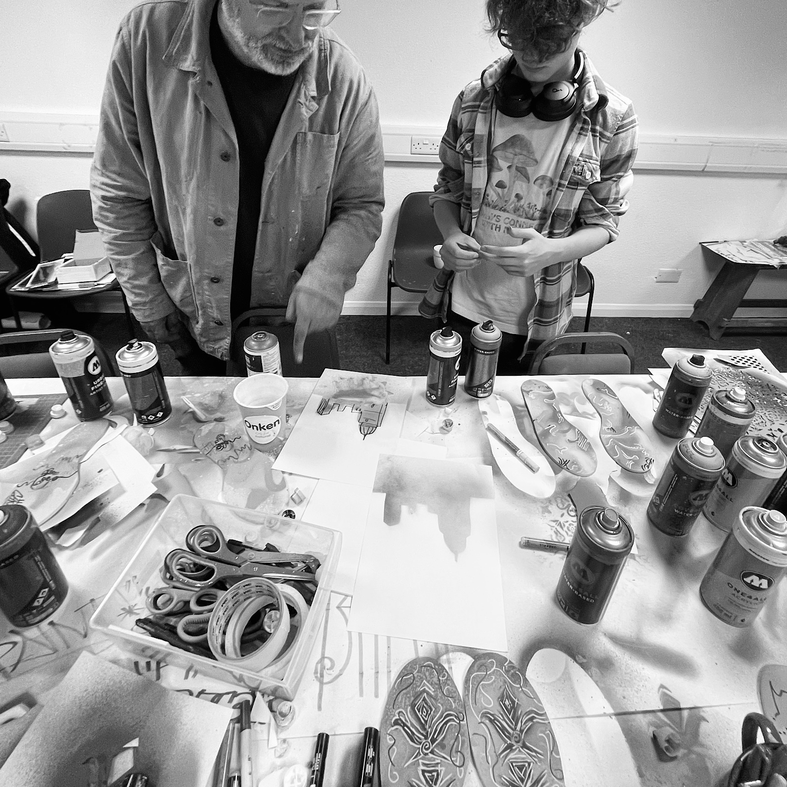 An artist and a young artist stand by a stable and look at materials and cans for spray painting