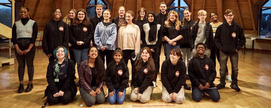 A group of young people stand for a group photo and they all look to the camera and smile