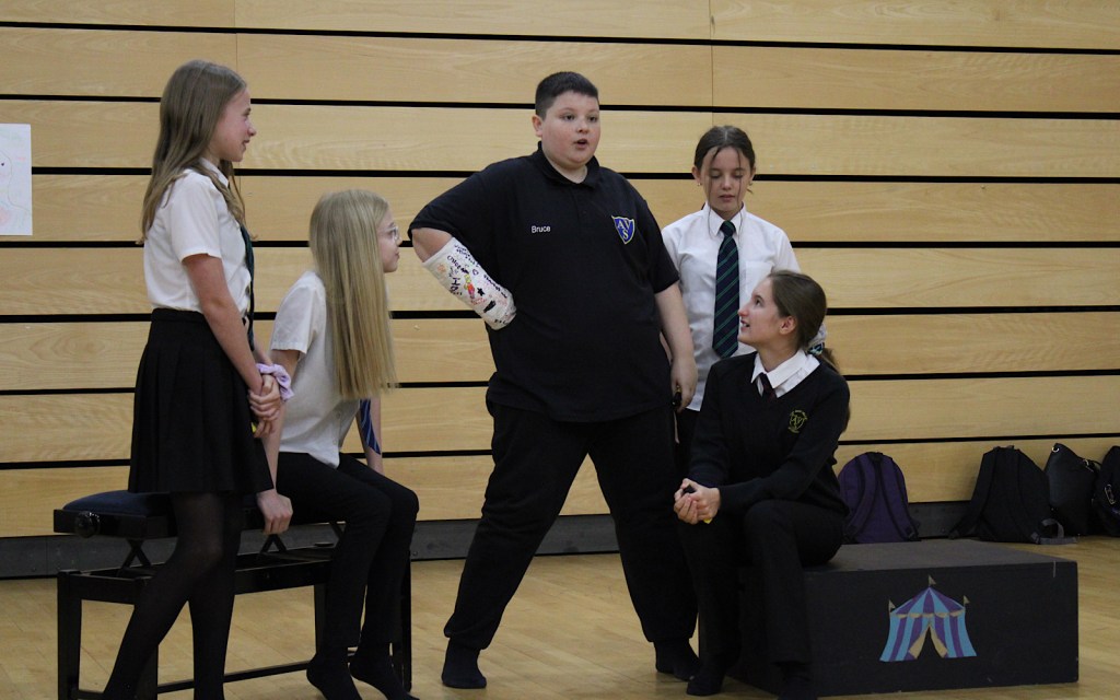 A group of five students in black and white uniform perform a scene as part of an art workshop