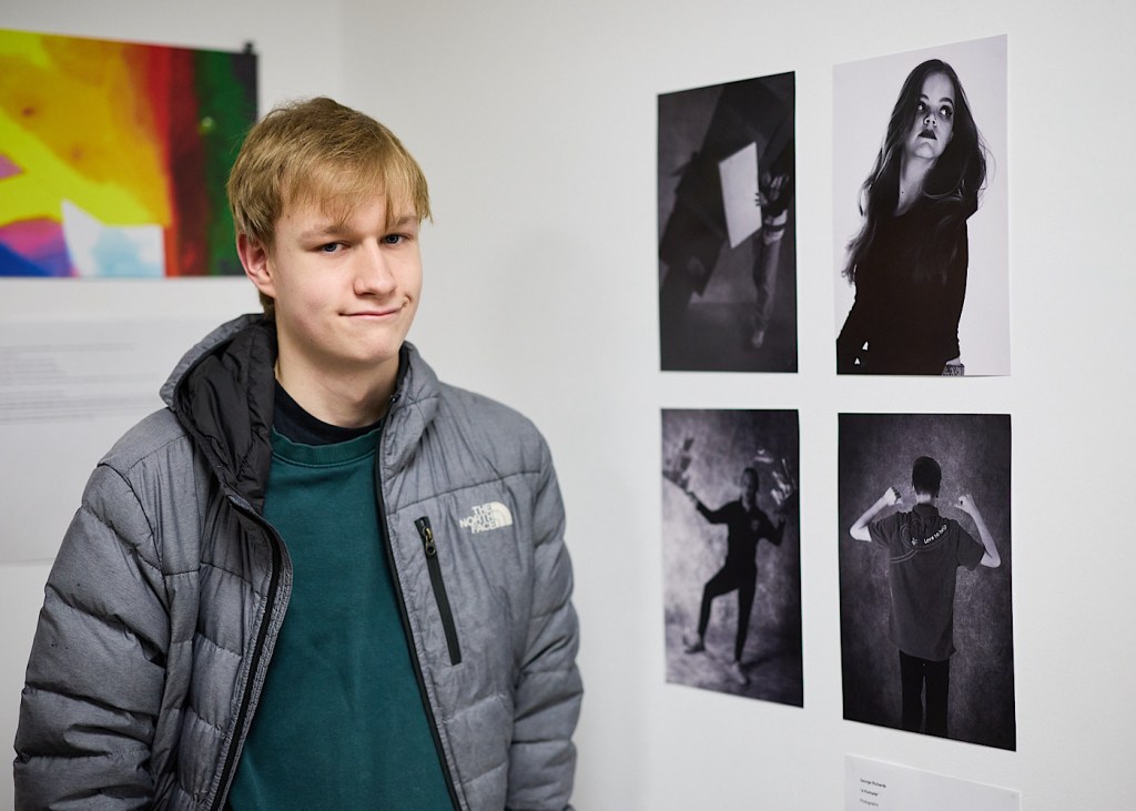 Four photography pieces on a wall form part of an exhibition and the artist stands in front