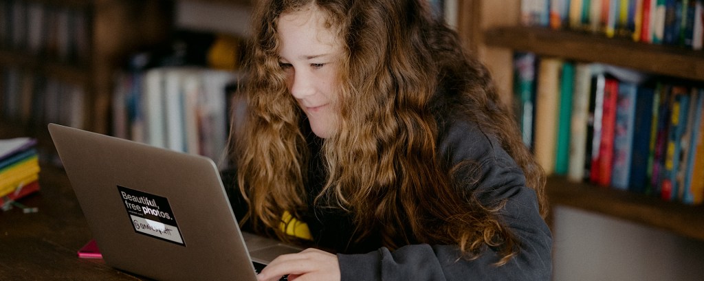 A young student sits at a laptop smiling
