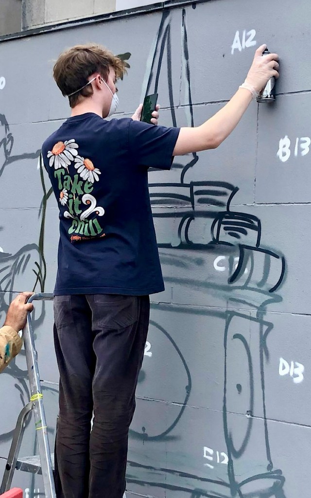 An artist stands on a ladder to spray paint a mural
