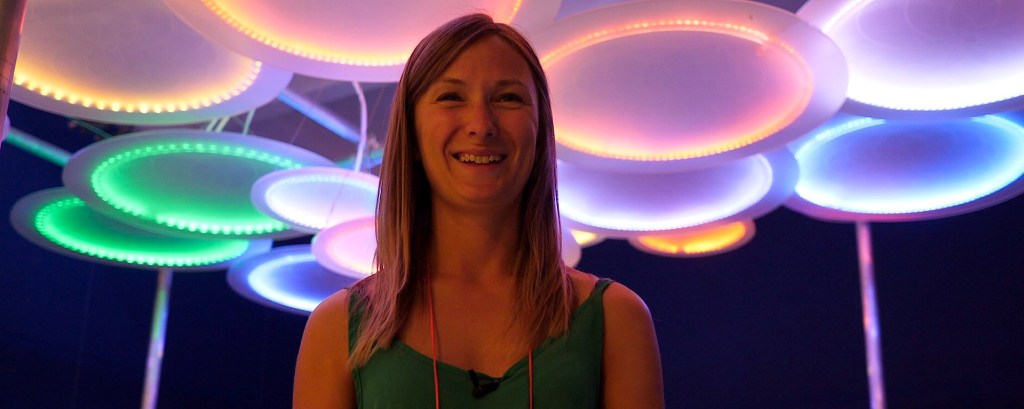 An artist stands in front of her art installation which is made of illuminated circles