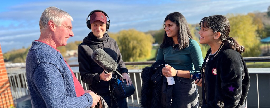 Two podcast hosts interview the Head of Automation at the RSC on a balcony in the theatre that overlooks the river