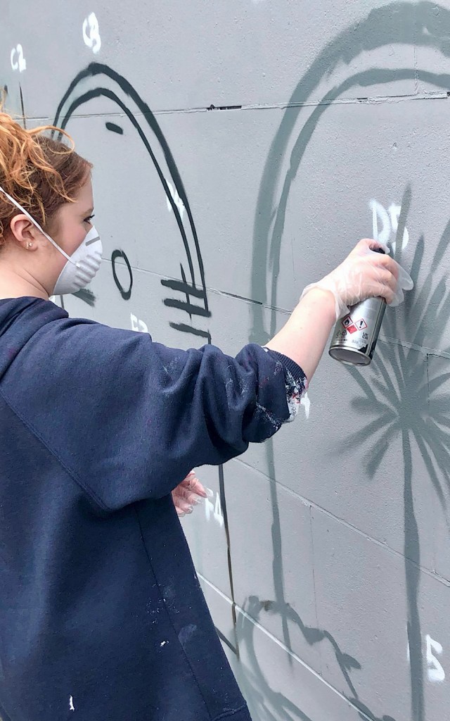 An artist holds a spray can against a wall to create a flower