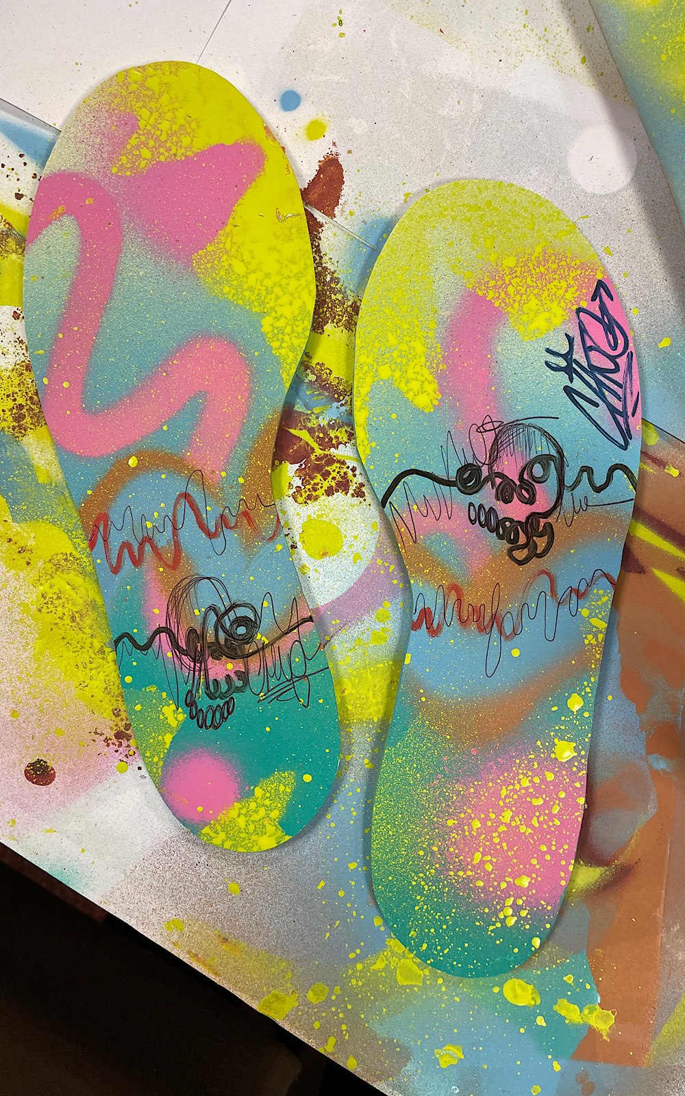 Canvases shaped like footprints have pink, yellow and black drawings on