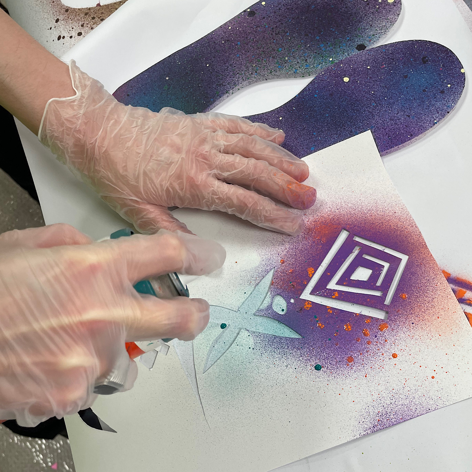 An artist uses a spray paint can to paint blue over a stencil they have made