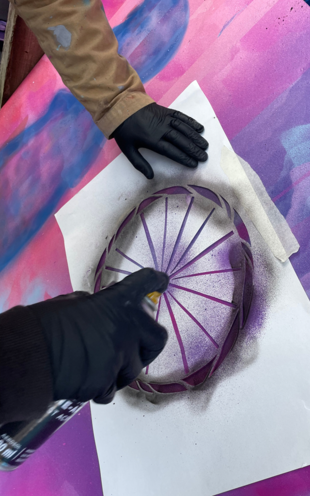 An artist spray paints a circle on a piece of purple paper