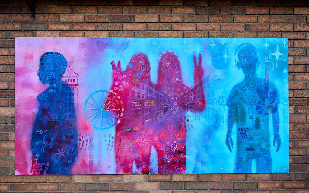A pink and purple mural is made up of shapes of people and images of a town in the background
