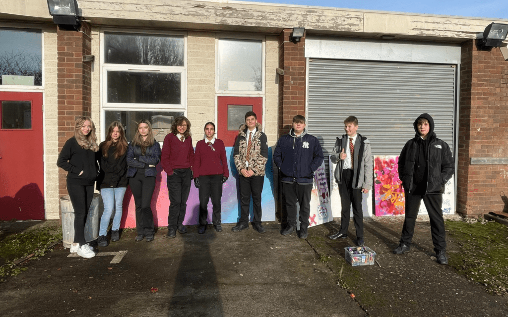 A group of school students stand in front of pieces of art
